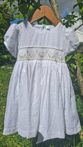 Robe à smocks en plumetis blanc et broderie dorée